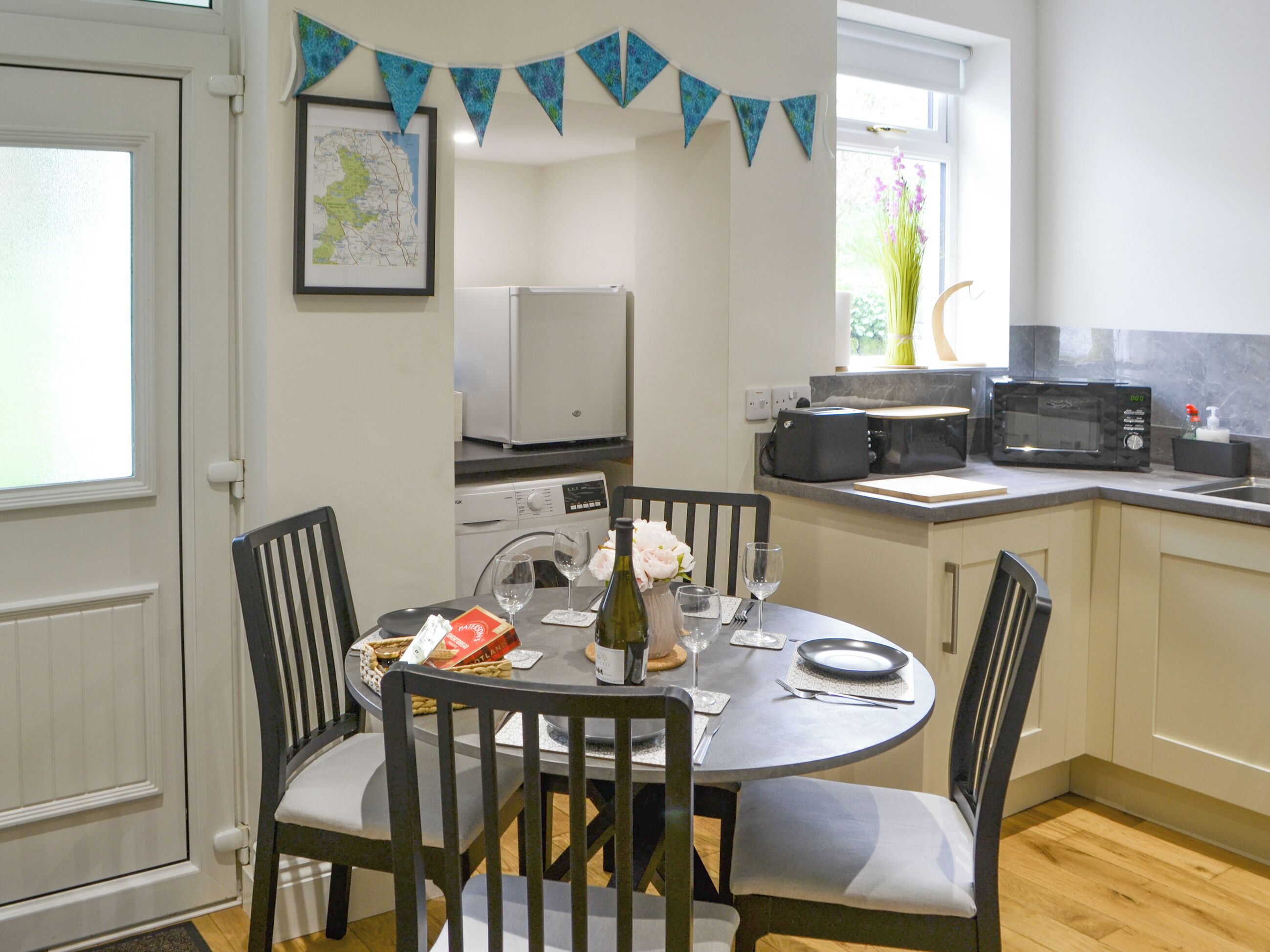A dining area with a round table, chairs, a map on the wall, and kitchen appliances.