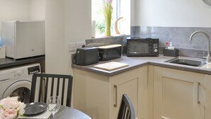 Una cocina compacta con microondas, tostadora y lavamanos. Hay una mesa de comedor con sillas y un jarrón de flores.
