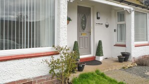 Una casa blanca con puerta gris, una ventana con persianas y un pequeño jardín con macetas.