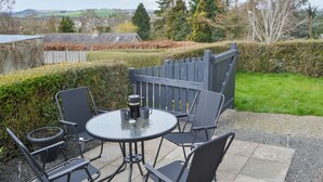 Un patio exterior con una mesa redonda y sillas, una cafetera y vistas al campo.