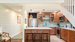 Una cocina moderna con armarios de madera, una isla central con taburetes, un refrigerador de acero inoxidable y un microondas.