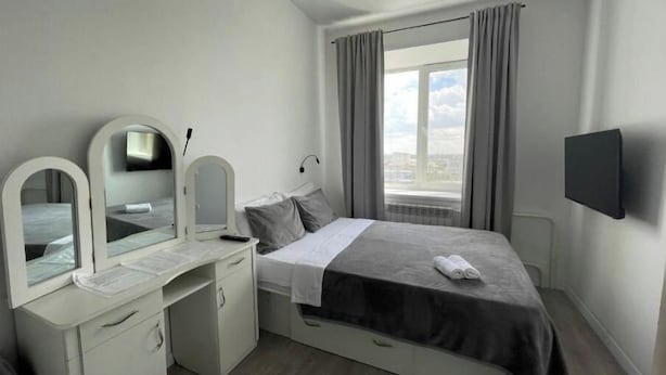 A modern bedroom with a bed, a desk with a mirror, and a TV.