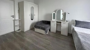 A bedroom with a wardrobe, a vanity with mirrors, a bed, and a bedside table.