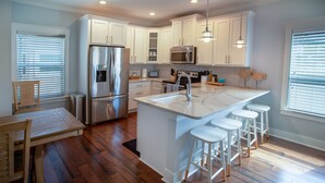 A modern kitchen with white cabinets, stainless steel appliances, a marble island with bar stools, and wooden flooring. - Townhome Steps to the Beach-Hot Tub, Private Yard (Jacksonville Beach)
