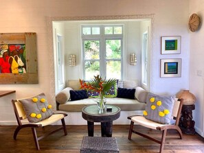 A room with a sofa, two chairs, a round table with a vase, and a window with a view of greenery.