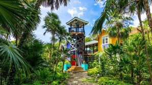 Um resort tropical com uma torre central, um caminho de pedra e vegetação exuberante.