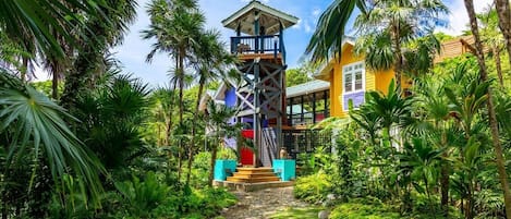 A tropical resort with a central tower, a stone pathway, and lush greenery.