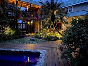 A two-story building with a wooden deck, a small pond, and tropical plants.