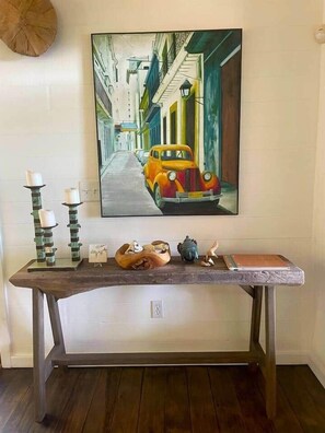 Pintura de uma cena urbana com um carro antigo, uma mesa de madeira com velas e objetos decorativos.