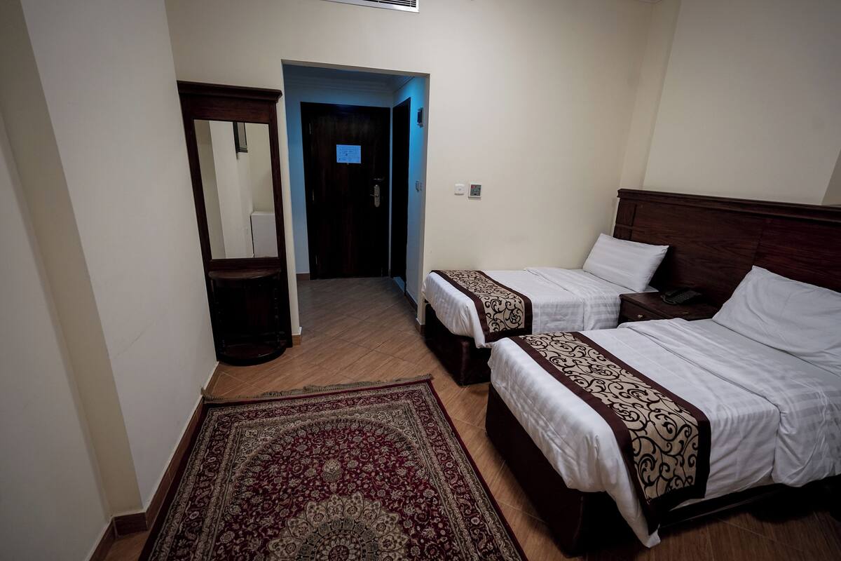 Een hotelkamer met twee bedden, een houten vloer, een rood tapijt met patroon en een spiegel.