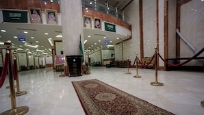Un hall d’entrée spacieux, doté d’un tapis rouge, d’une grande colonne et de portraits encadrés accrochés au mur.