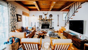A cozy living room with a stone fireplace, wooden furniture, and a large TV.