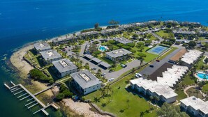 Vista aérea de una zona residencial costera con varios edificios, un muelle y un mar azul y transparente.