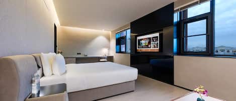 A modern hotel room with a bed, a desk, a TV, and a view of the city.