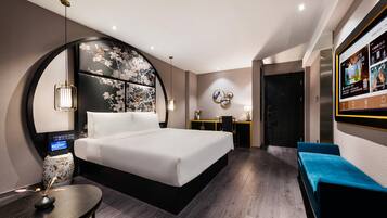 Una habitación de hotel moderna con una cama grande, un escritorio, una zona de estar y un televisor en la pared.