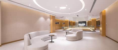 Un moderno vestíbulo de hotel con una zona de estar curva, una vitrina de vidrio y una lámpara central.