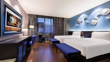 Habitación de hotel con cama, escritorio, silla, banco y televisor en la pared.