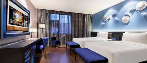 Une chambre d’hôtel avec un lit, un bureau, une chaise, un banc et un téléviseur fixé au mur.