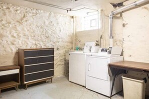 Compact laundry room with a washing machine and dryer, a wooden cabinet, and a trash bin.