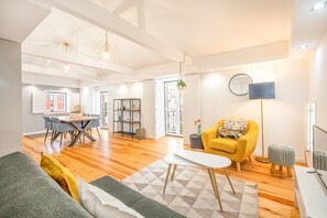 Uma sala de estar espaçosa com uma mesa de jantar, uma poltrona amarela e um candeeiro de chão moderno.