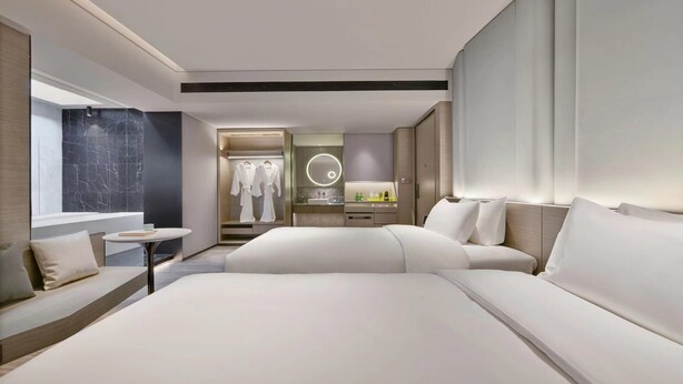 A modern hotel room with a large bed, a sitting area with a small table, and a bathroom with a vanity and mirror. - Blossom Hill Hotel Yangzhou Slender West Lake (Yangzhou)