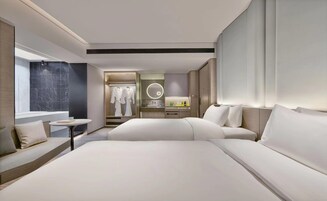 Una habitación de hotel moderna con una cama grande, un área de descanso con una mesita y un baño con tocador y espejo.