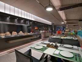 A modern restaurant with a buffet area, dining tables set with plates, cutlery, and napkins.