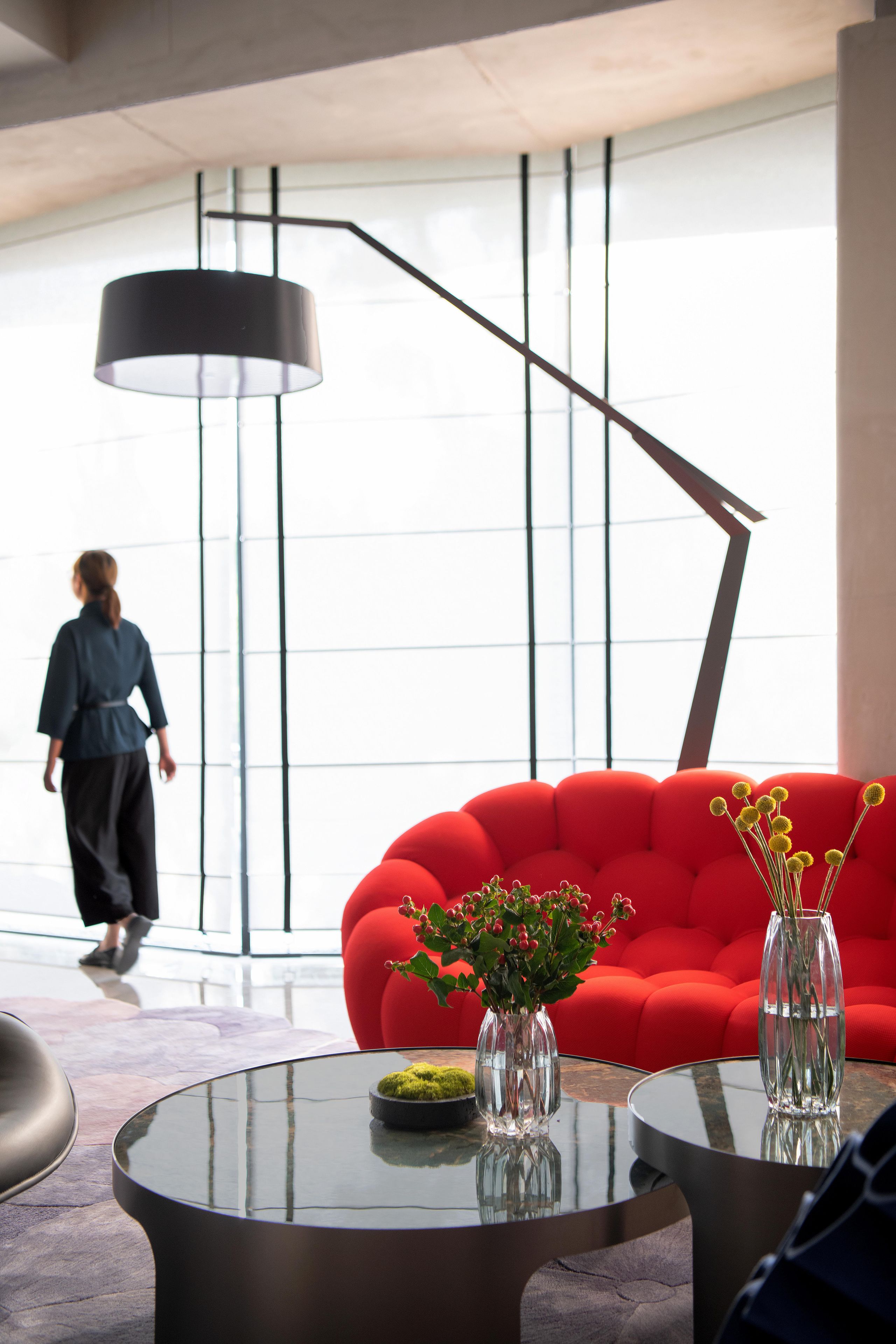 A modern interior with a red sofa, two glass vases with plants, and a round glass table.