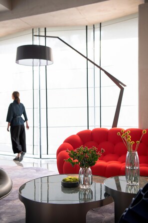 A modern interior with a red sofa, two glass vases with plants, and a round glass table. - Blossom Hill Hotel Yangzhou Slender West Lake (Yangzhou)