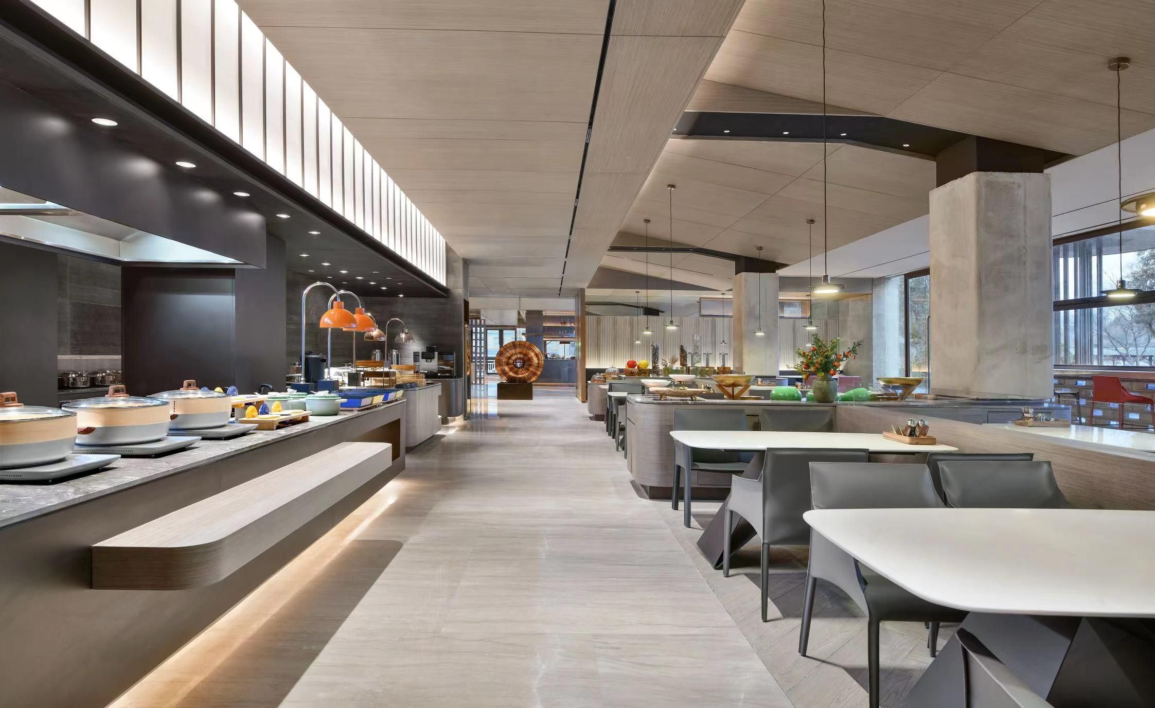 A modern restaurant with a long counter, multiple seating areas, and a central kitchen visible in the background.