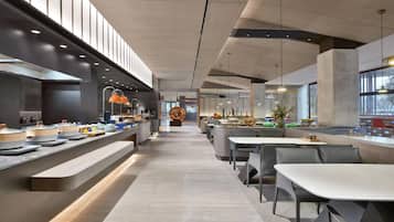 A modern restaurant with a long counter, multiple seating areas, and a central kitchen visible in the background.
