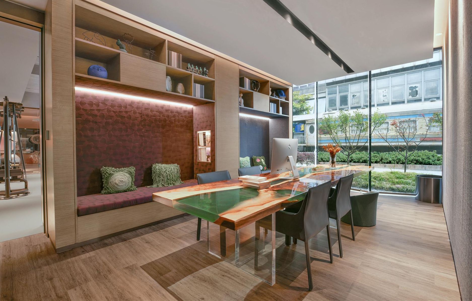 A modern office space with a glass-top table, chairs, a bookshelf, and a view of a train.