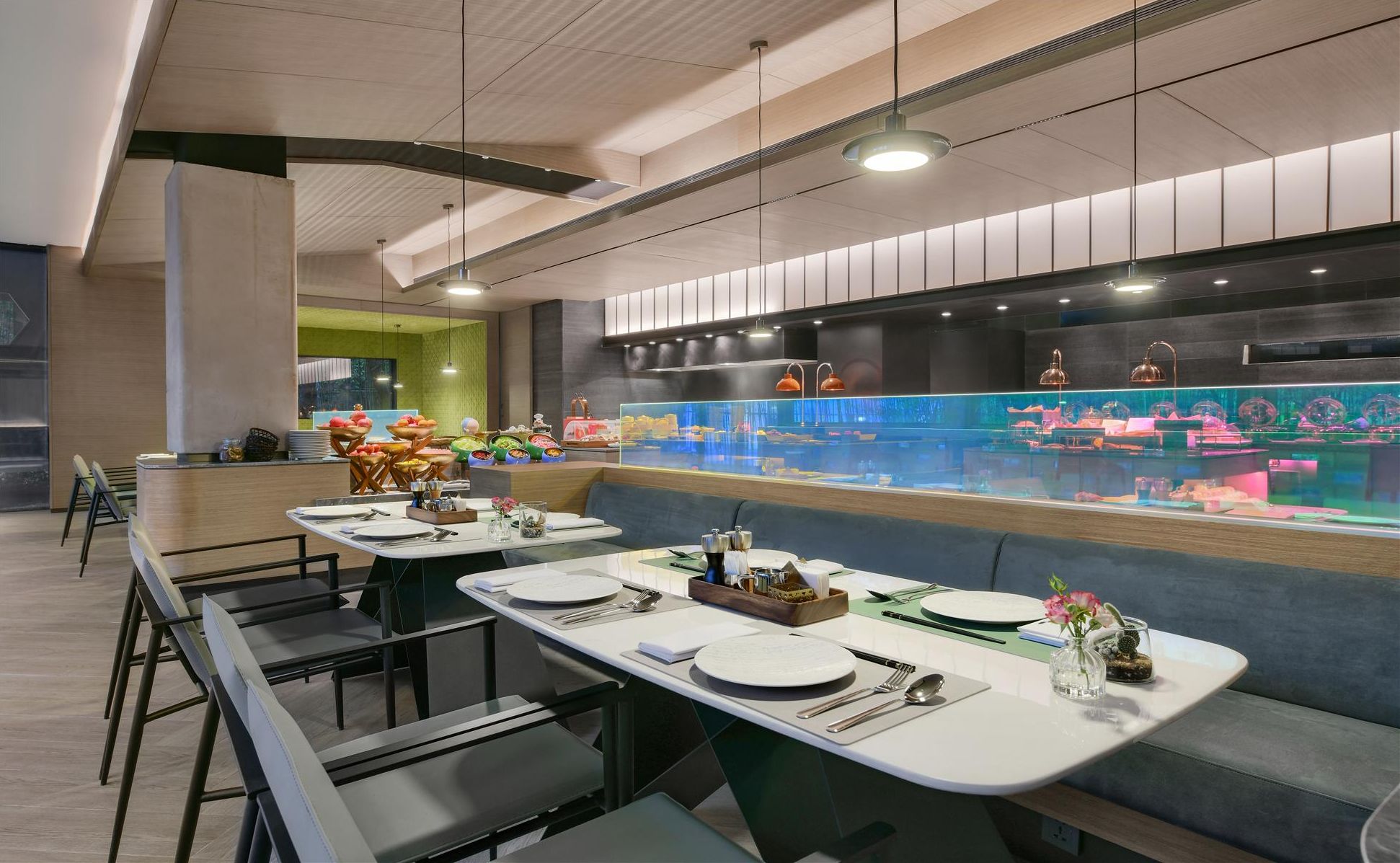 A modern restaurant with long communal tables, a central bar area, and a vibrant aquarium display.