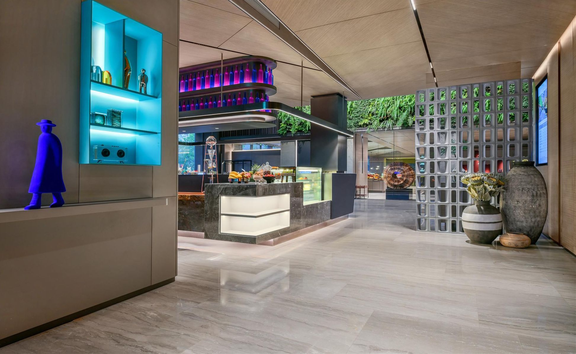 Un vestíbulo de hotel moderno con una barra central, una escultura azul decorativa y vistas al jardín exterior.