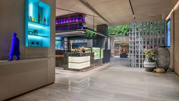 Un vestíbulo de hotel moderno con una barra central, una escultura azul decorativa y vistas al jardín exterior.