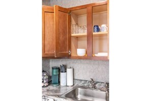 Kitchen area with open cabinetry, glass-fronted shelves, and a stainless steel sink.