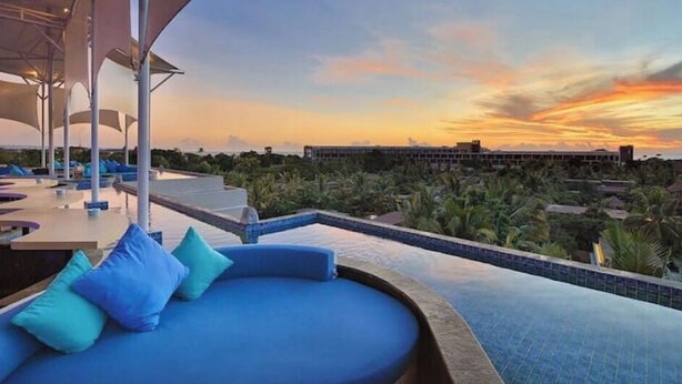 A rooftop pool area with blue lounge chairs and a view of the sunset over a residential area. - Double-Bedroom With Terrace In Seminyak (Bali)