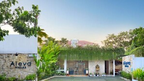 Un complejo de villas llamado Aleva Villas con fachada de piedra, un acceso cubierto y abundante vegetación.