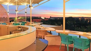 Un área de bar al aire libre con asientos y vistas al horizonte de la ciudad al anochecer.