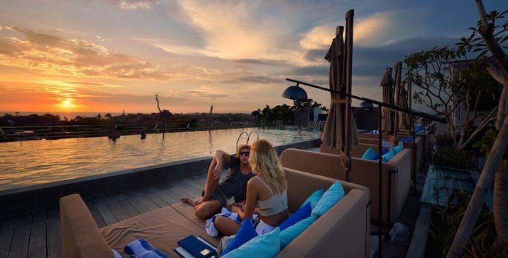 A sunset view from a rooftop pool area with lounge seating and a poolside bar.