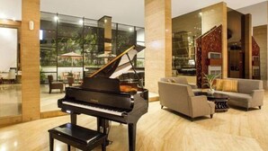 Un gran piano en un vestíbulo amplio con una decoración moderna, ventanas grandes y una zona de estar con sofás y una mesa de centro.