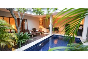 Un espace piscine intérieur moderne, avec des chaises longues, une petite table et un coin repas visible au fond.