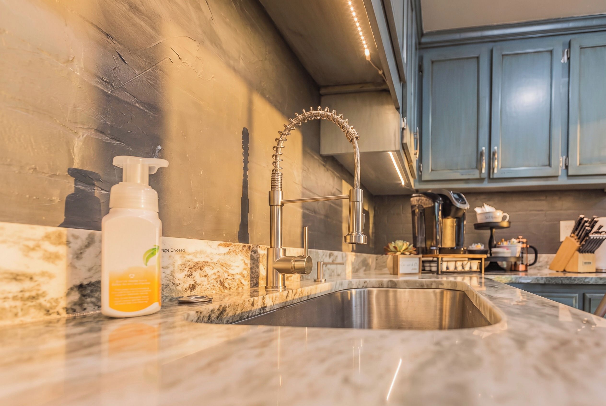 Una cucina con lavello in acciaio inossidabile, un erogatore di sapone e un rubinetto con tubo flessibile.