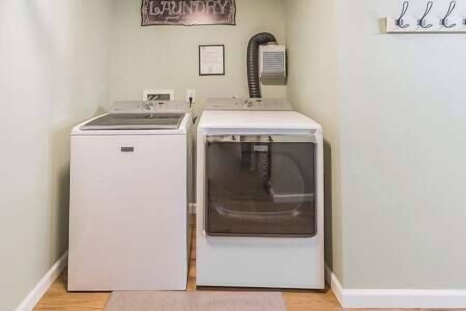 Una sala de bugaderia amb dues màquines blanques, un escalfador fixat a la paret i un cartell que diu "LAUNDRY".