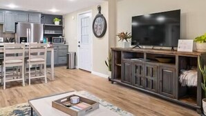 A modern living room with a flat-screen TV, wooden cabinets, and a dining area with chairs.