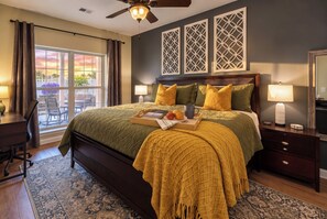 A bedroom with a large bed, two bedside lamps, a ceiling fan, and a view of the outdoors through a window.