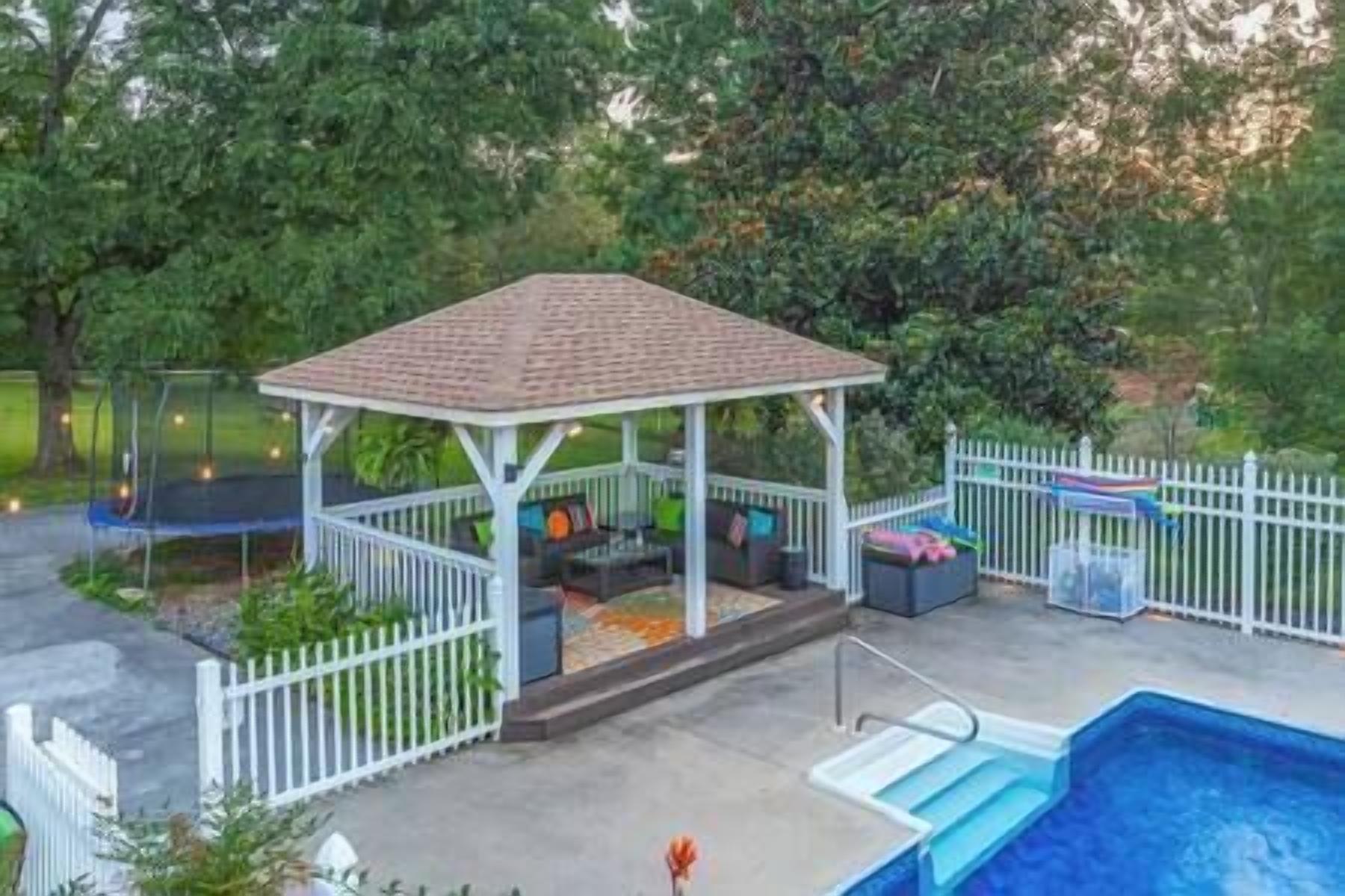 A covered patio area with seating, a pool, and a fenced yard.