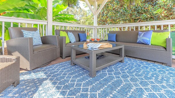 A covered outdoor seating area with wicker furniture and a patterned blue rug.