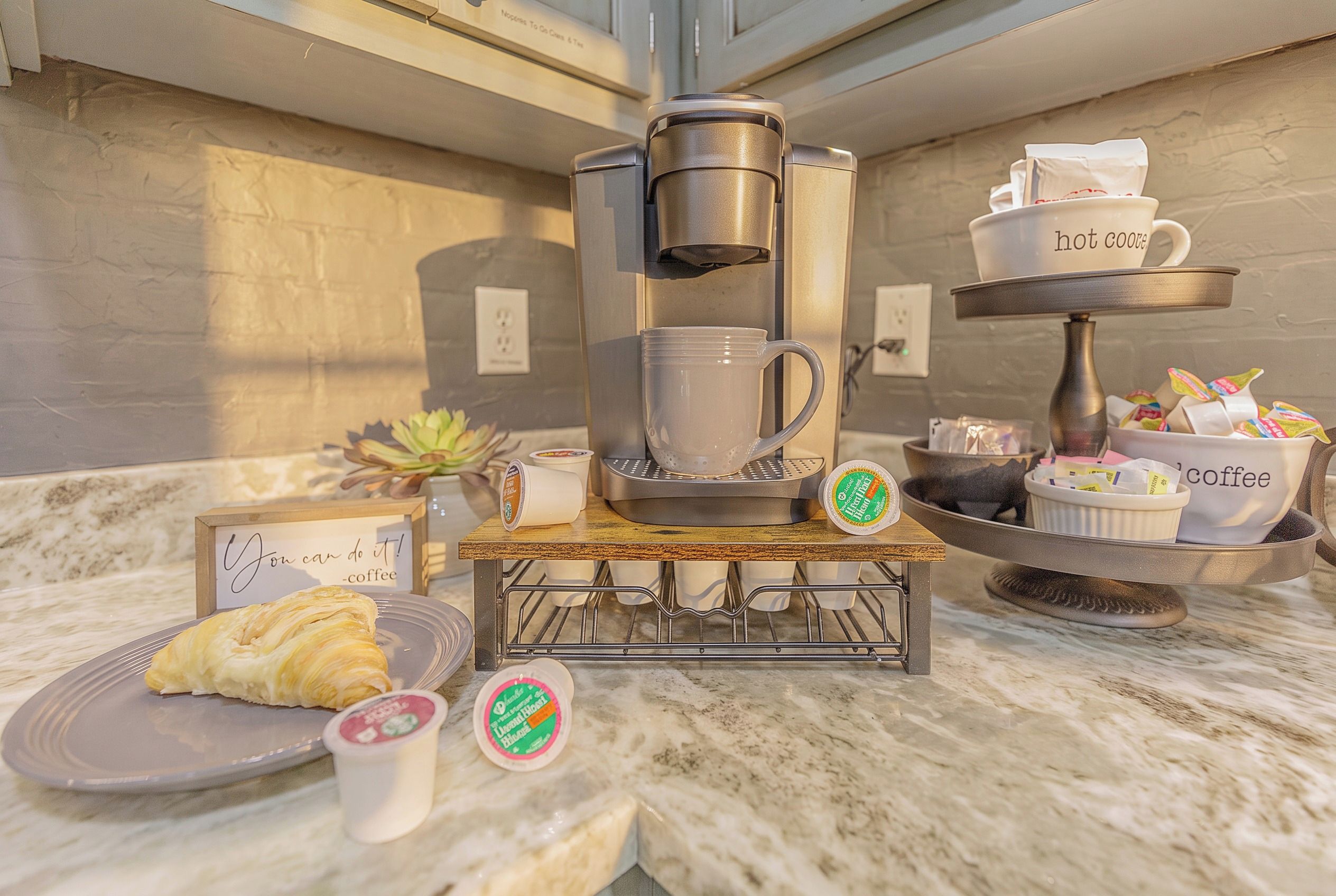 A kitchen counter with a coffee maker, a plate with a pastry, and a coffee cup.