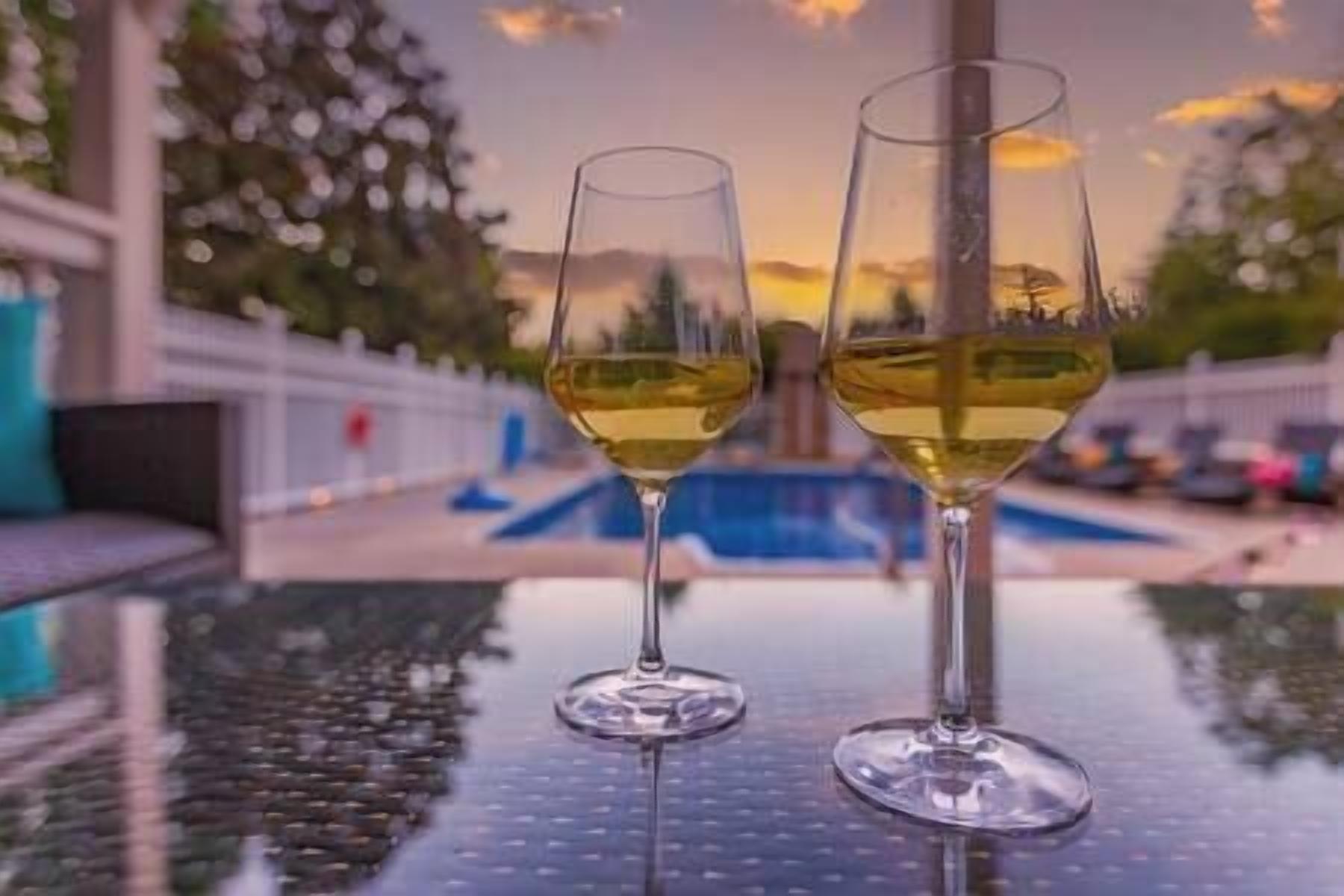 Two wine glasses on a table with a pool in the background.